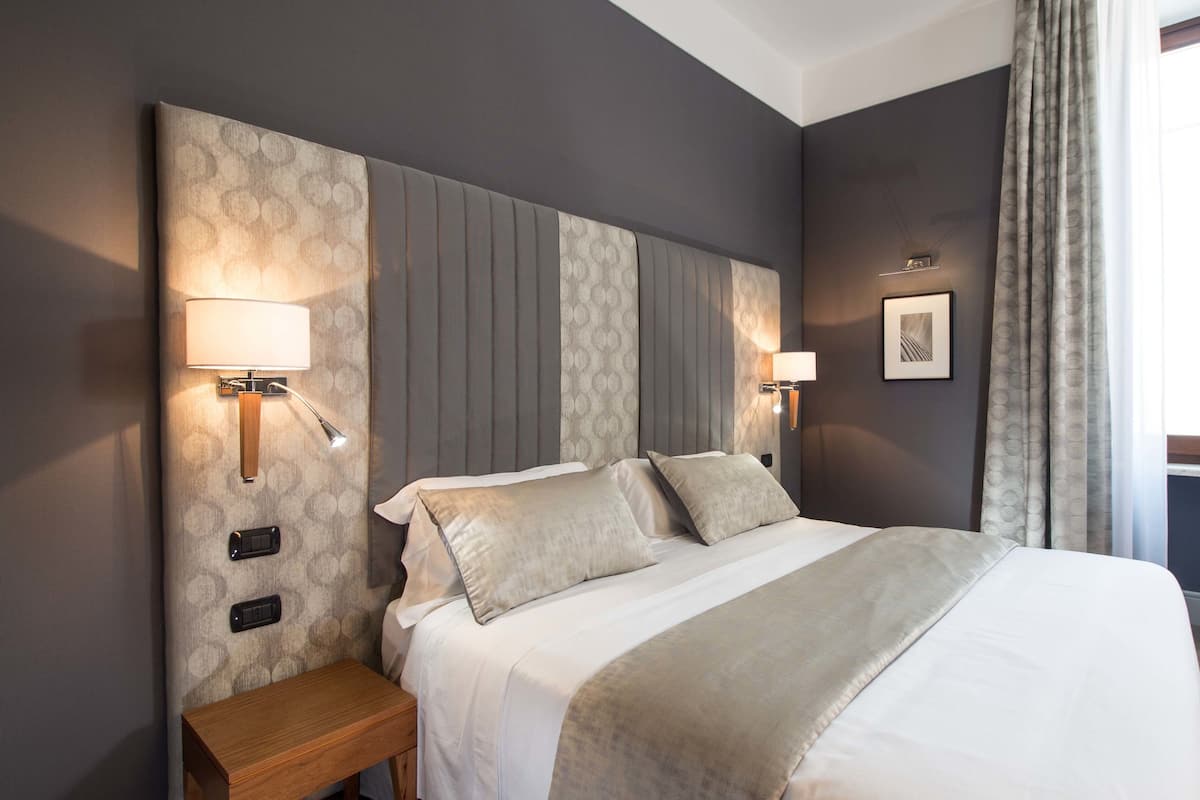 Une chambre d’hôtel avec un grand lit, deux lampes de chevet, une table de chevet et une fenêtre avec des rideaux.