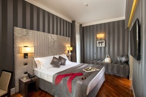 Ett hotellrum med en stor säng, sänglampor, ett litet sidobord, en läshörna med en soffa och en TV som är monterad på väggen.