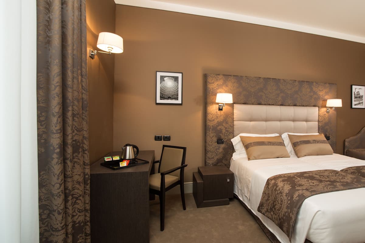 Une chambre d’hôtel avec un grand lit, un bureau doté d’une bouilloire et deux lampes fixées au mur.