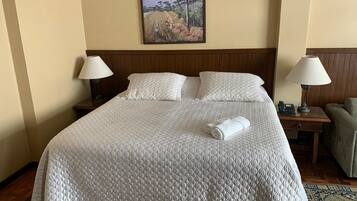 A neatly made bed with a quilted white cover, two bedside lamps, a painting on the wall, and a small table with a lamp.