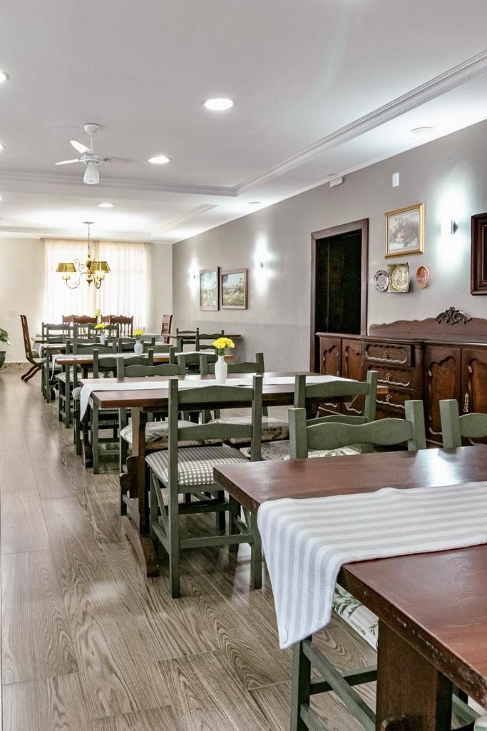A dining area with multiple tables and chairs, a chandelier, and a wooden cabinet.