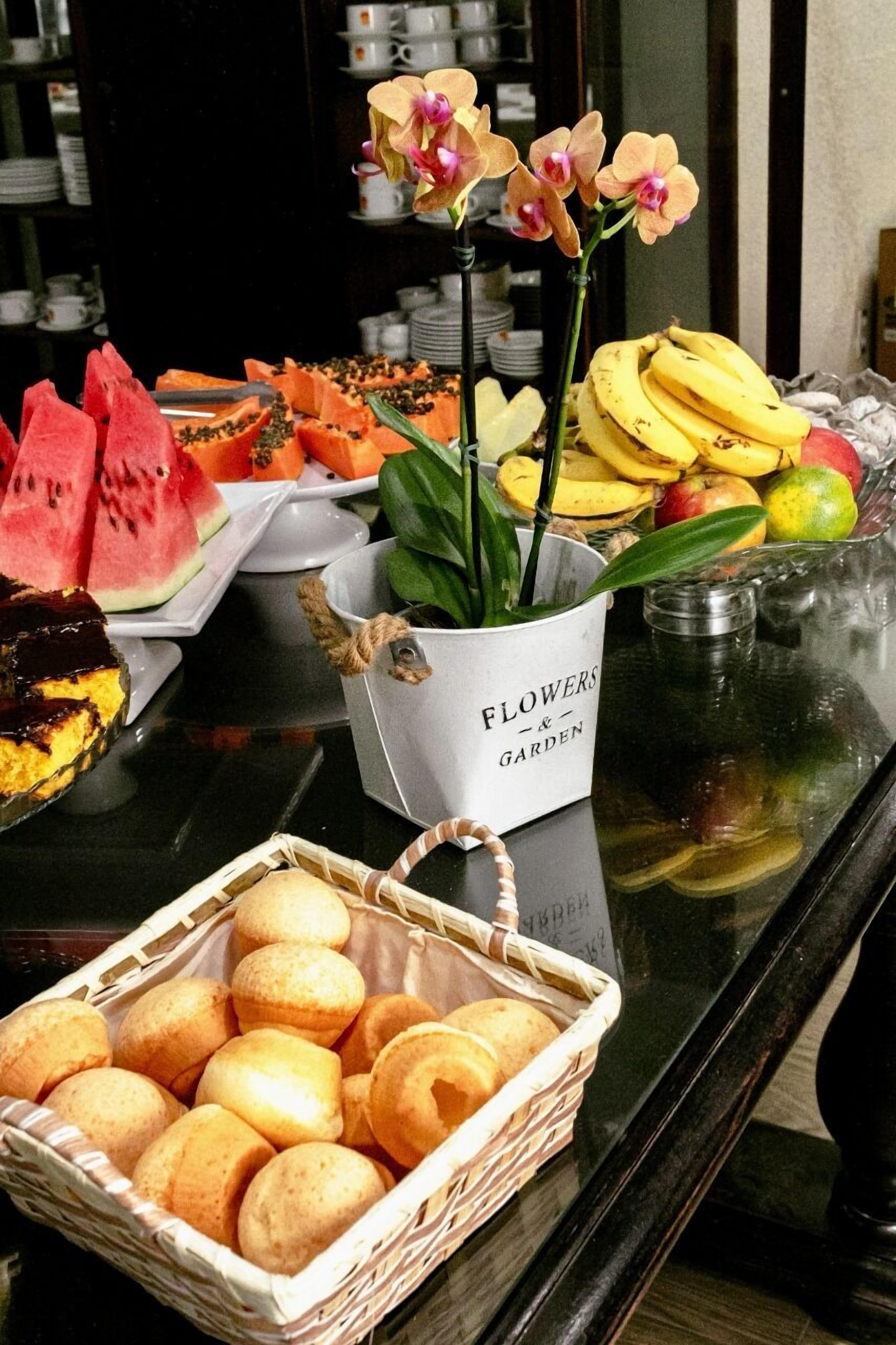 A buffet table with various fruits, a basket of pastries, and a flower arrangement.