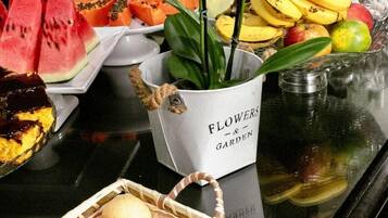 Mesa de buffet com diversas frutas, uma cesta de pastelaria e um arranjo floral.