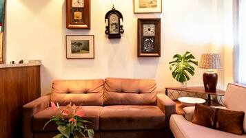 Una sala de estar con un sofá marrón, una mesa de centro de cristal con una planta y cuadros en la pared.