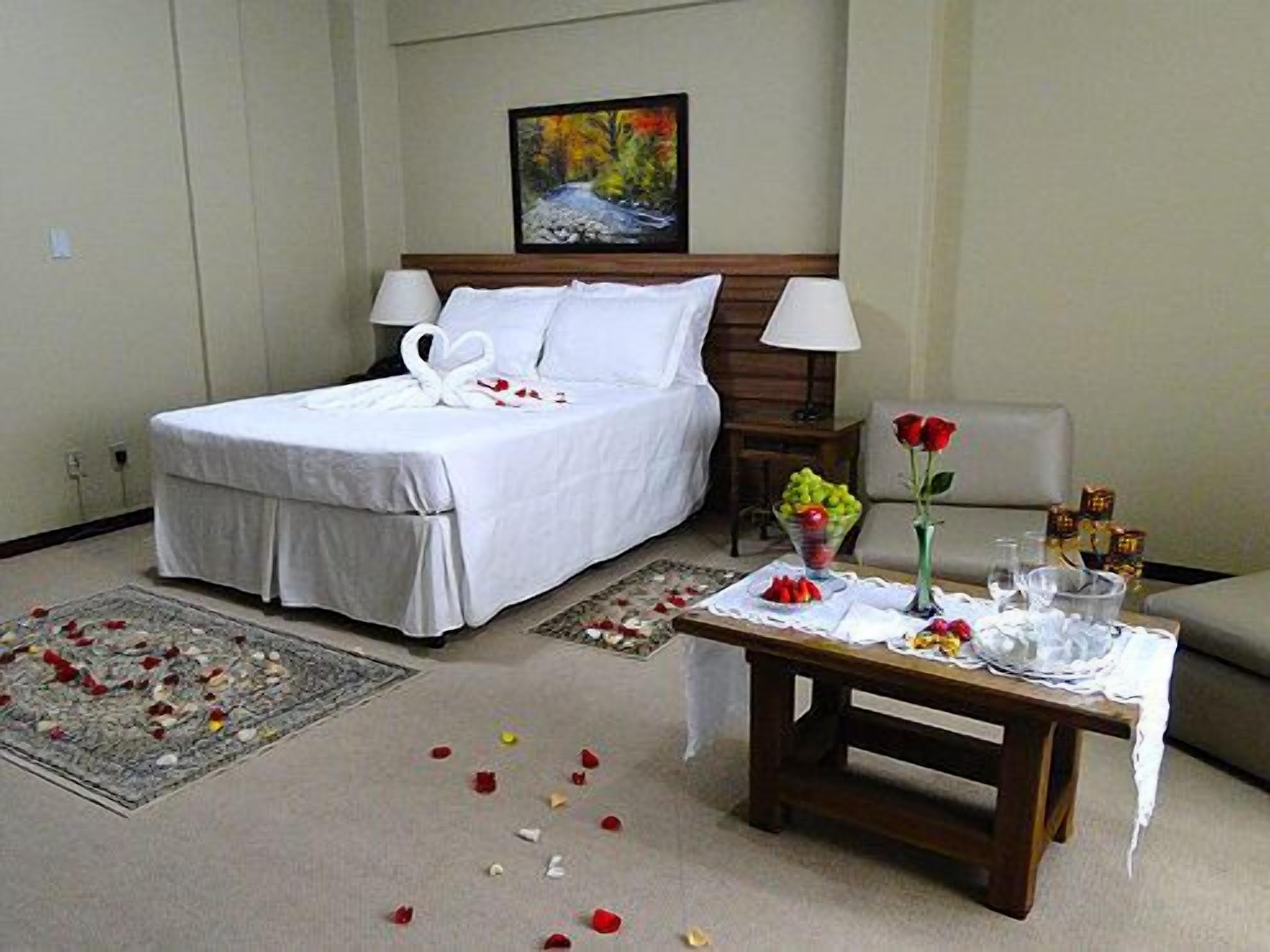 Habitación de hotel con una cama bien tendida, una mesita de noche con un jarrón de flores y un cuadro en la pared.