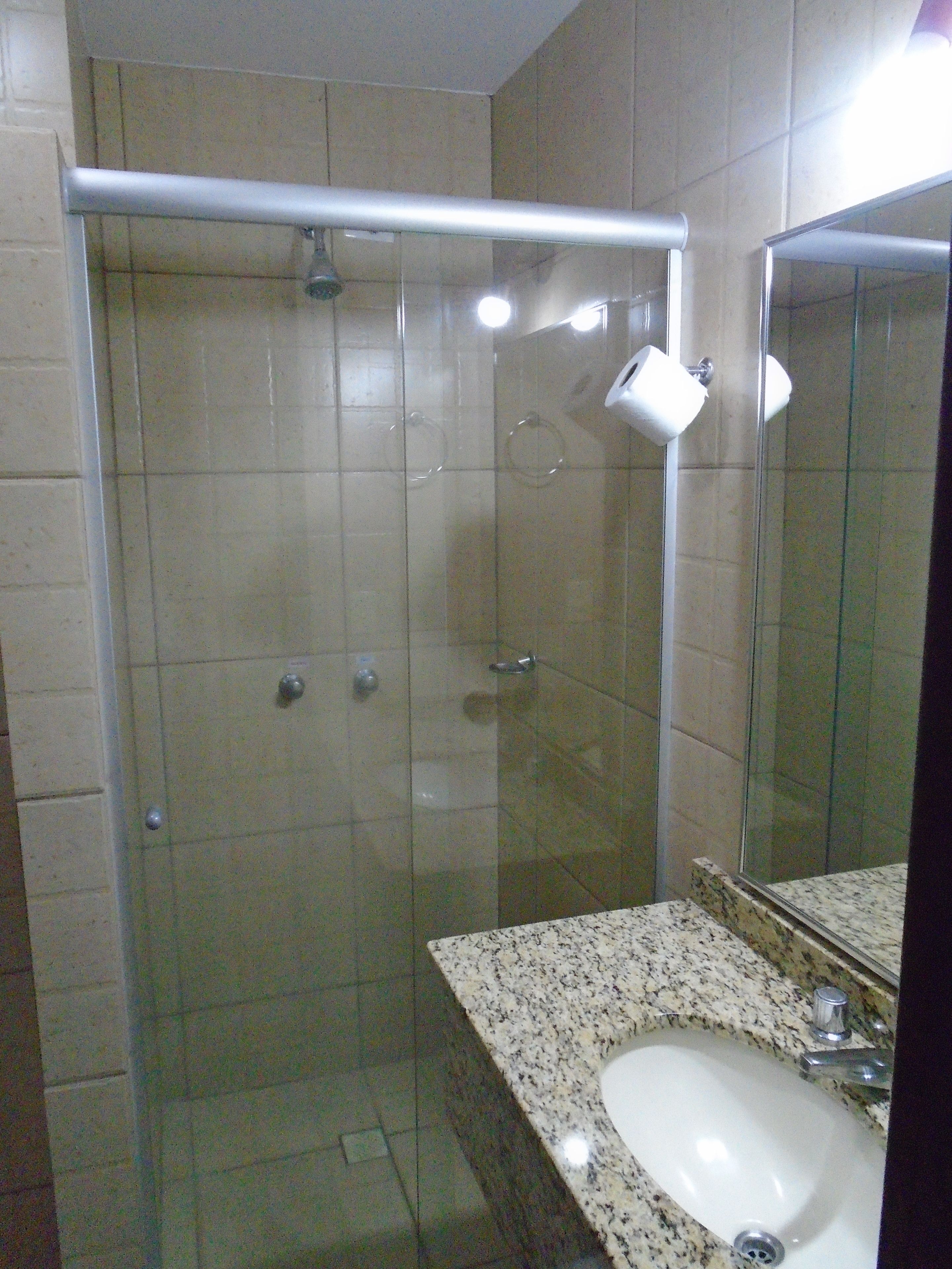 Un baño con ducha de vidrio, lavamanos con encimera de granito y un espejo.