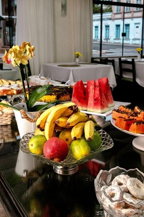 A buffet table with various fruits, including bananas, apples, and watermelon slices, and a bowl of donuts. - Hotel San Rafael (Porto Uniao)