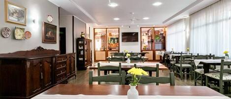 A dining area with tables and chairs, a wooden cabinet, and a vase with flowers on a table.