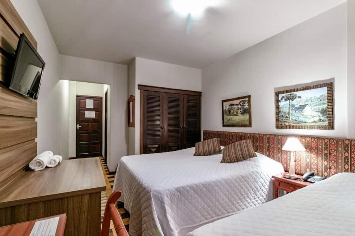 Ett hotellrum med två sängar, ett skrivbord med en stol, en tv som är monterad på väggen och en dörr som leder till ett annat rum.