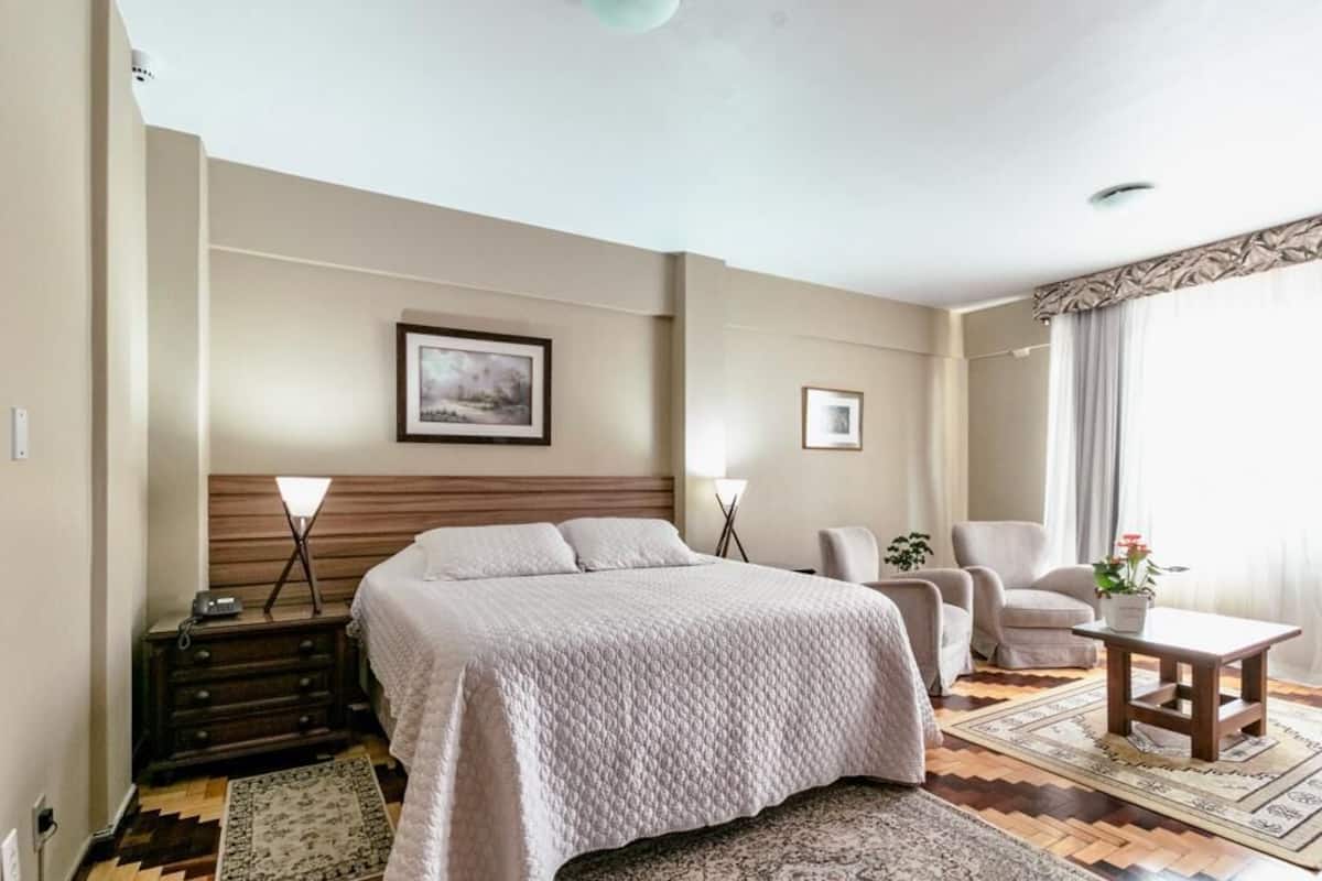 Ett hotellrum med en stor säng, ett skrivbord, en stol, en soffa och ett litet bord med en växt.