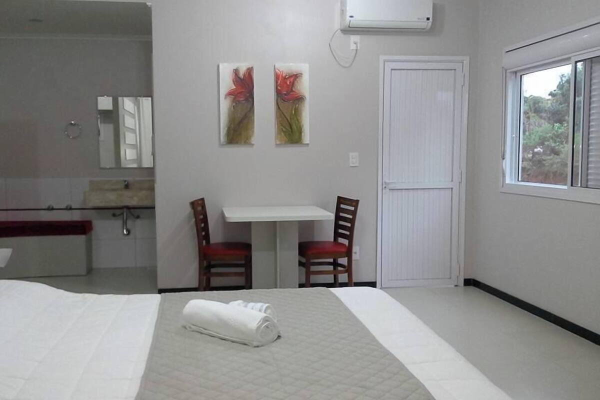 A hotel room with a bed, a small table with two chairs, a window, and a door.