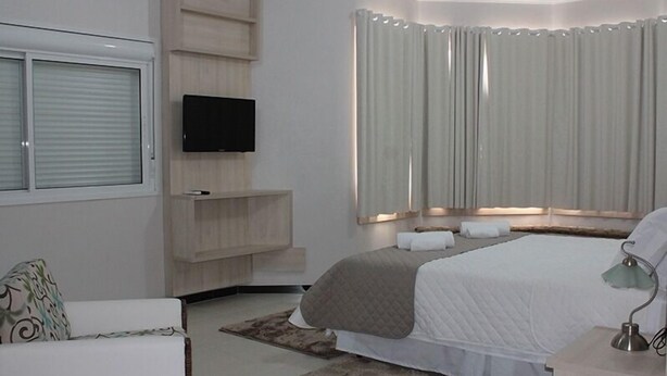 A modern bedroom with a bed, a TV, a built-in shelf, and a window with curtains. - Hotel Bell Sttar (Marau)