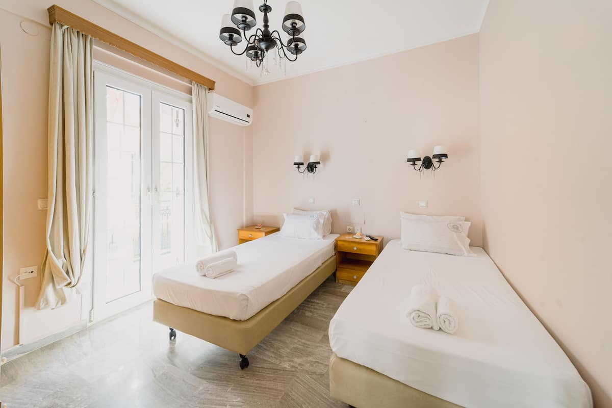 Habitación de hotel con dos camas, un candelabro, un equipo de aire acondicionado y vistas al exterior.