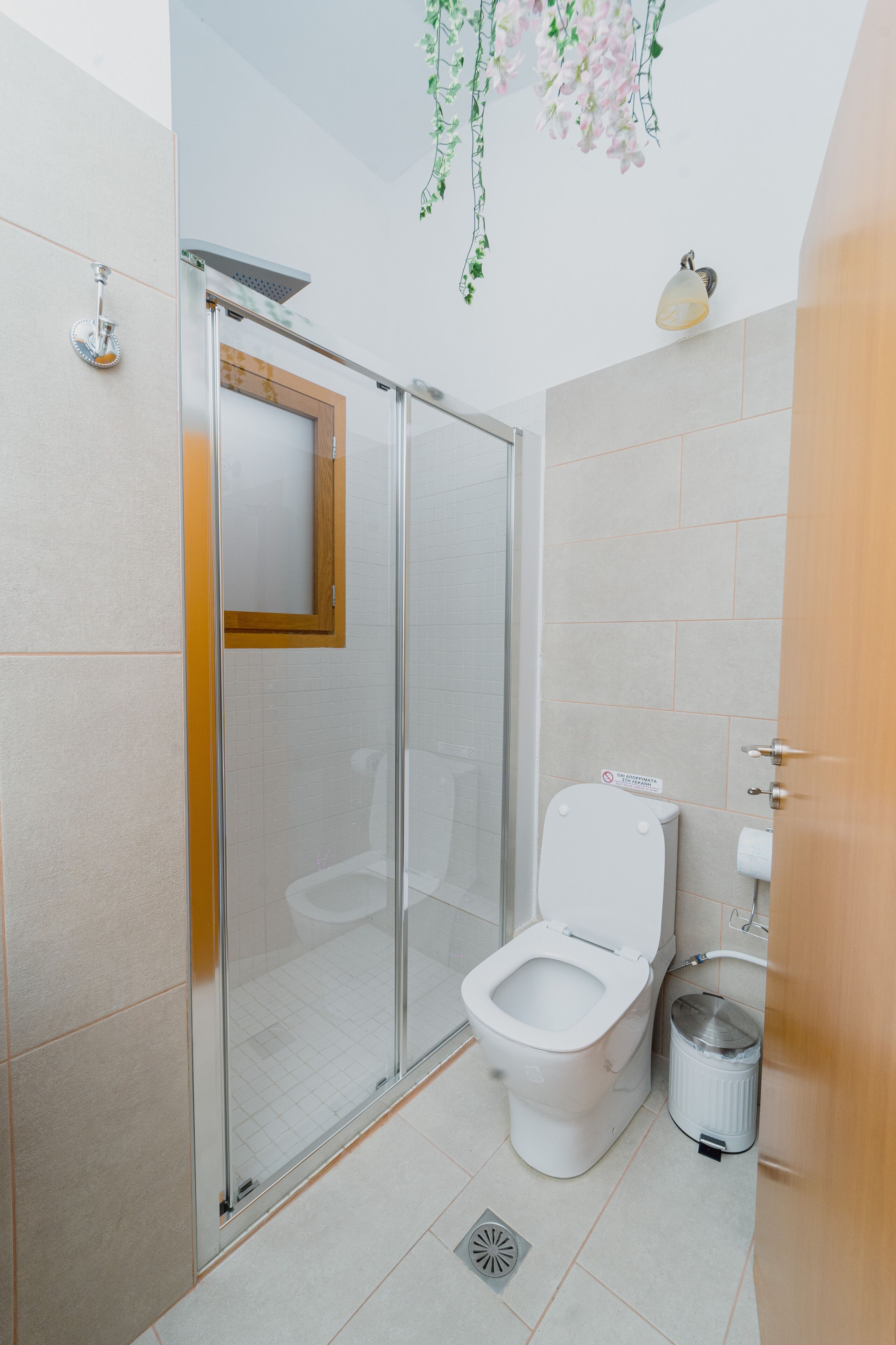 A modern bathroom with a glass-enclosed shower, a toilet, and a trash bin.