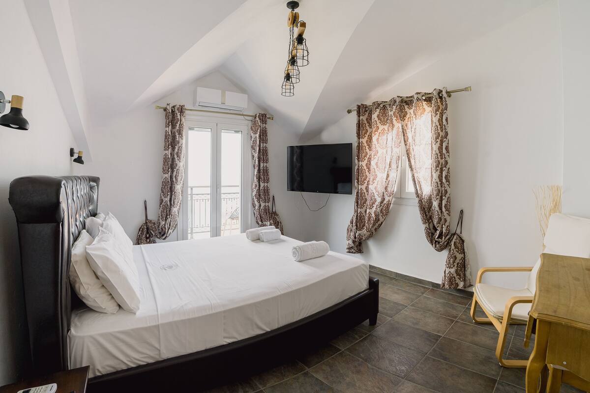 Un dormitorio con cama, cómoda de madera, silla, televisor y cortinas estampadas.