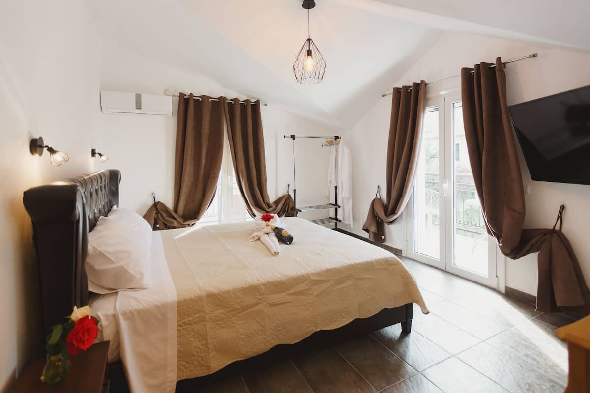 Habitación de hotel con una cama grande, un televisor de pantalla plana y un balcón con cortinas.