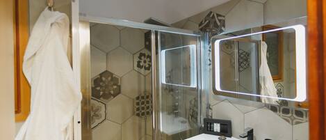 Un baño moderno con cabina de ducha de vidrio, un lavabo blanco y un espejo grande.