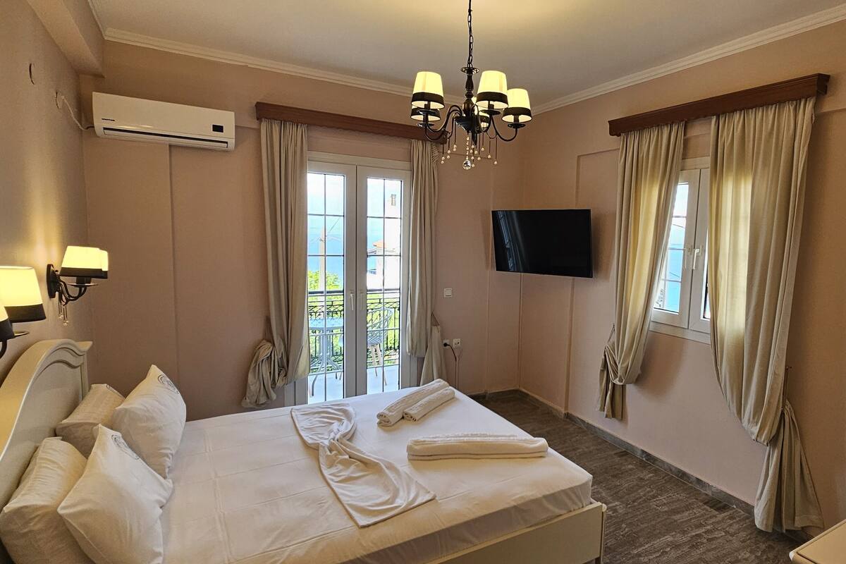 Habitación de hotel con cama, televisor, escritorio y vista al balcón.