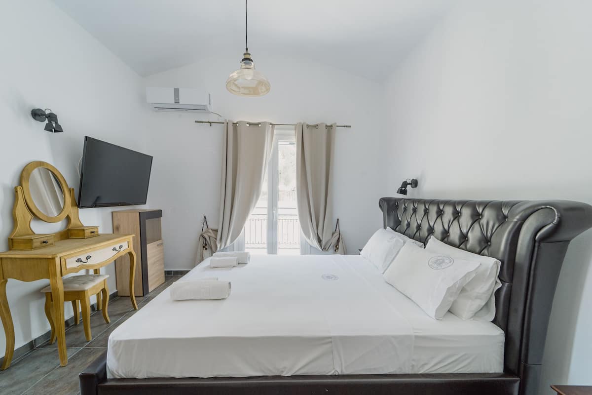 Un dormitorio con cama, escritorio, silla, televisor y ventana con cortinas.