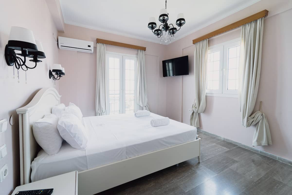 Una habitación de hotel con cama, televisor montado en la pared y aire acondicionado.