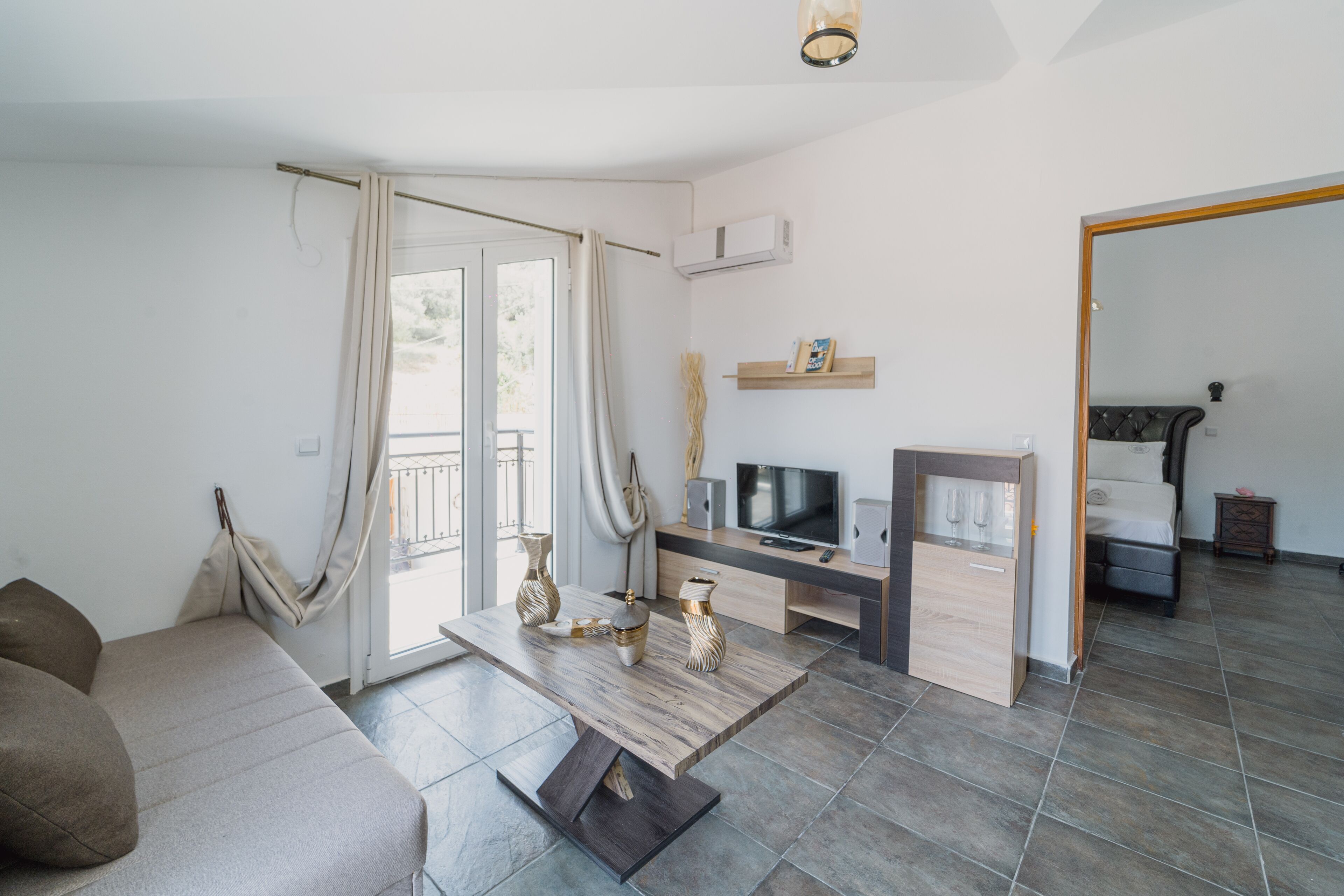 A modern living room with a sofa, a coffee table with decorative items, a TV, and a small cabinet.