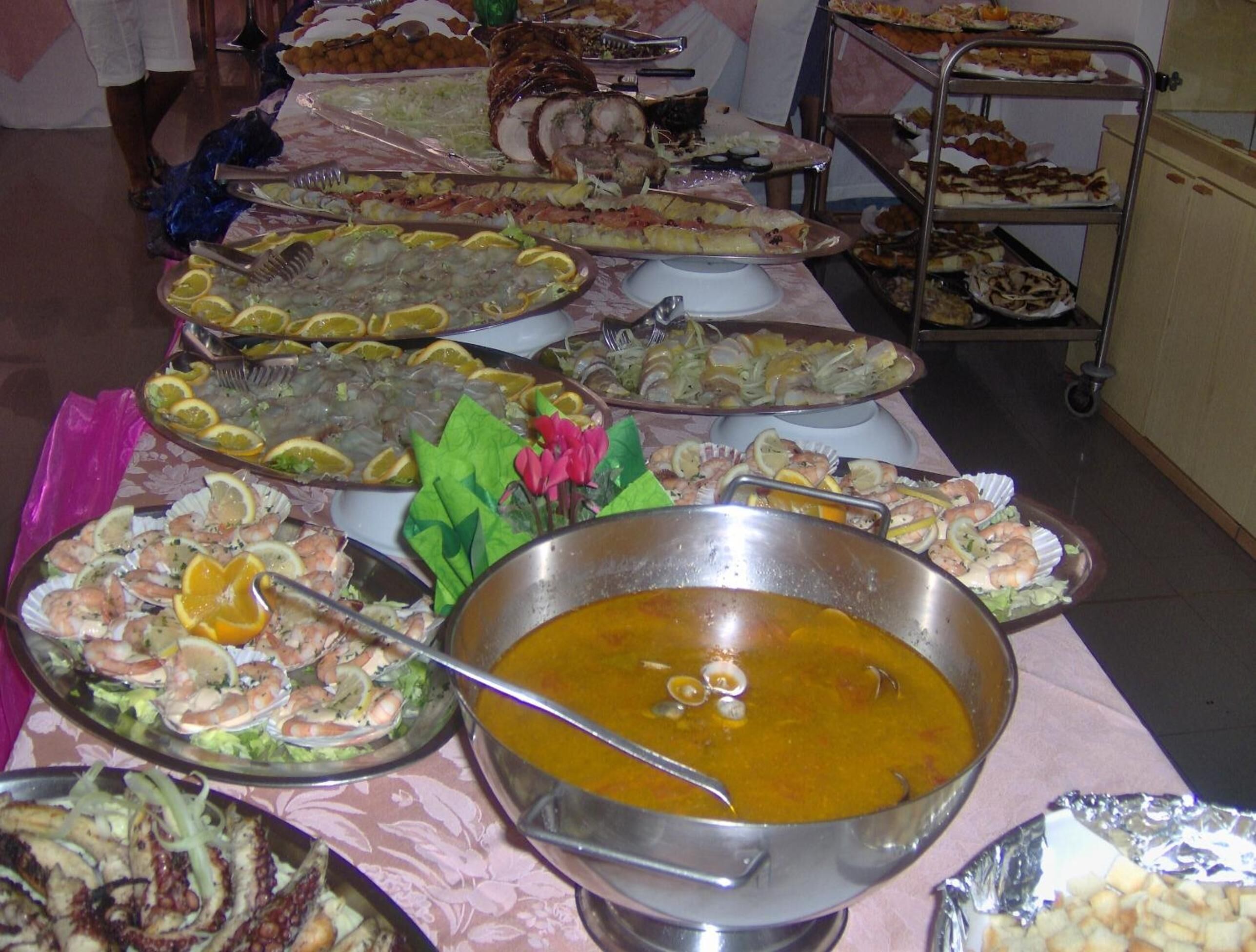 A buffet table with various seafood dishes, including shrimp, scallops, and grilled fish, along with a large bowl of soup.