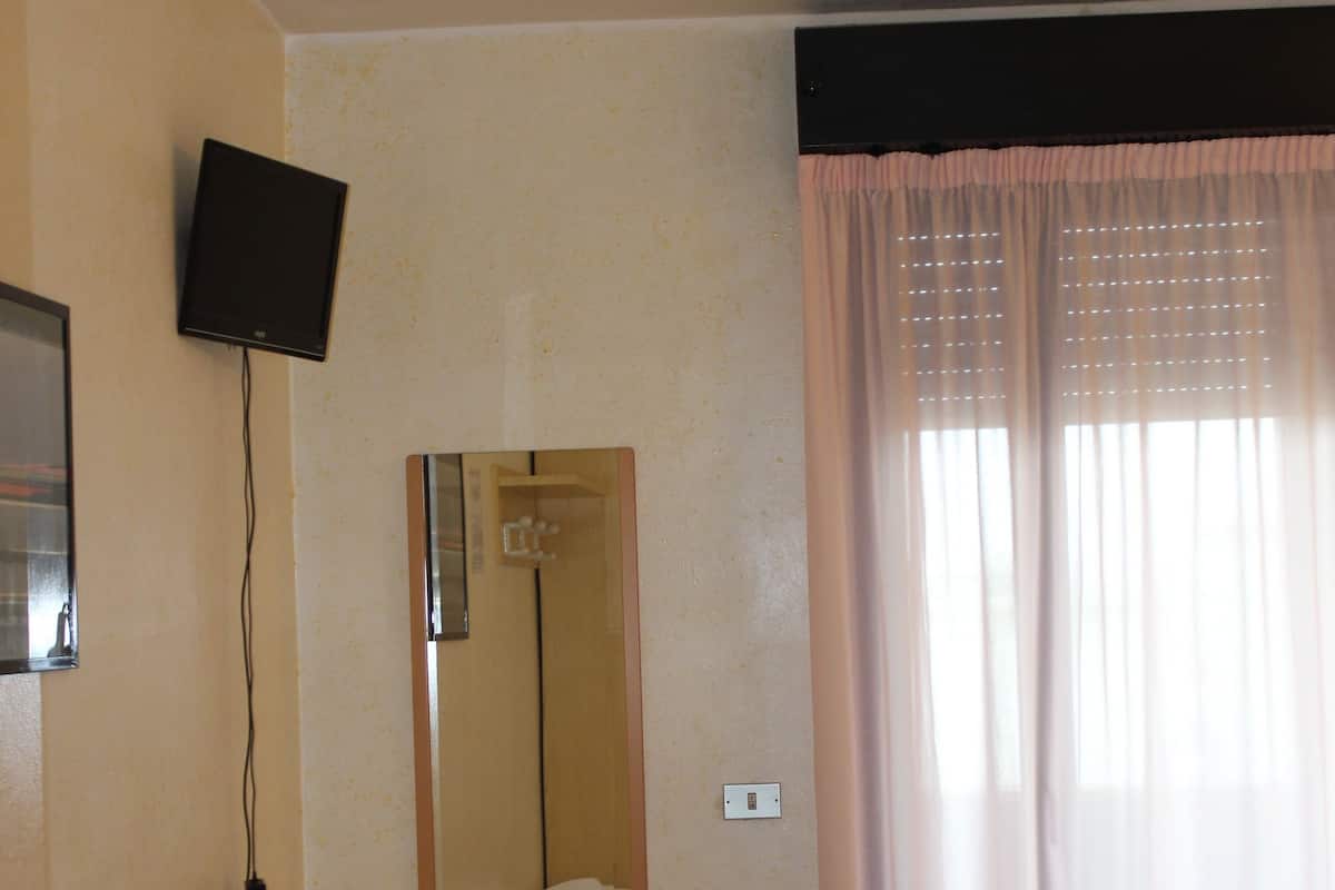 A hotel room with a bed, a desk, a chair, a television mounted on the wall, and a window with curtains.