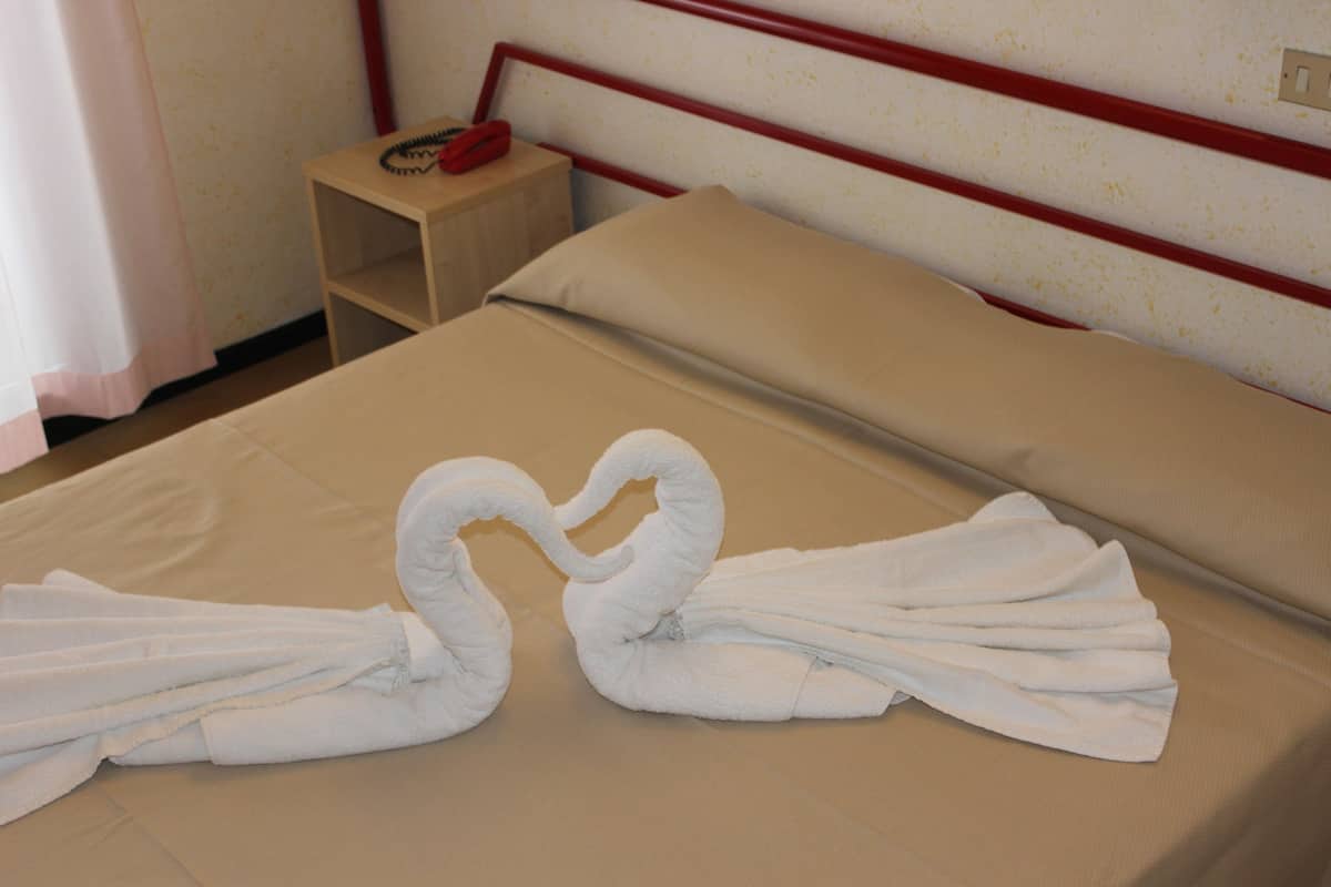 A neatly made bed with two towels arranged in a swan shape.
