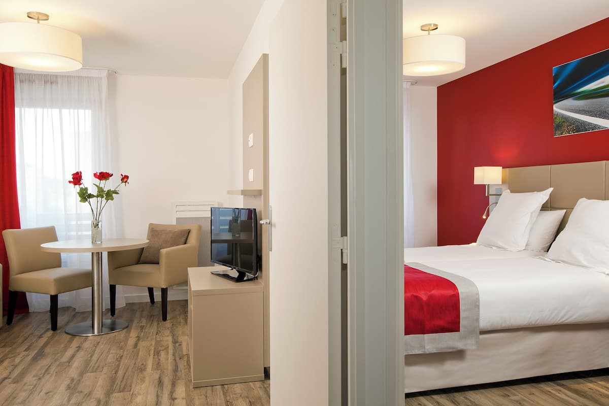 A hotel room with a bed, a desk with a computer, a chair, and a table with a vase of flowers.