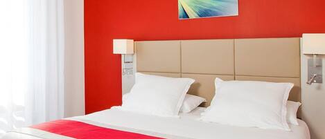 A hotel room with a red accent wall, a large bed with white bedding, and a modern abstract painting above the bed.