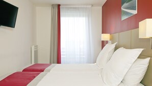 Een hotelkamer met twee bedden, een aan de muur bevestigde televisie, een raam met gordijnen en twee bedlampjes.
