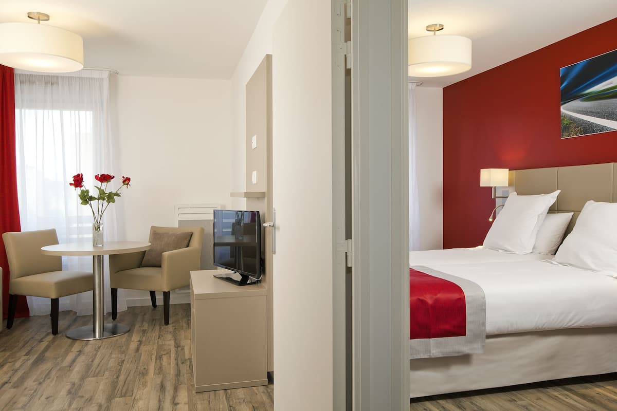 A hotel room with a bed, a desk with a computer, a chair, and a table with a vase of flowers.