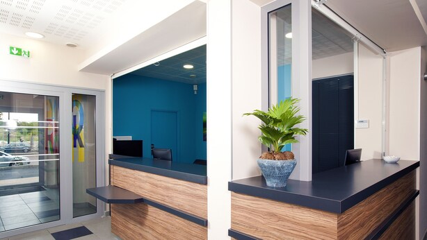 Een receptiebalie met een blauwe wand en een houten toonbank. Er staat een potplant op de toonbank.