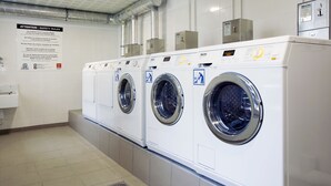 Een rij witte wasmachines met voorlaadklep in een commerciële wasserette, met een bord waarop veiligheidsregels staan.