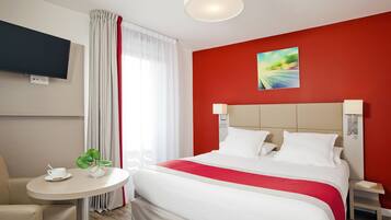 A hotel room with a bed, a TV, a small table with a cup and saucer, and a plant.