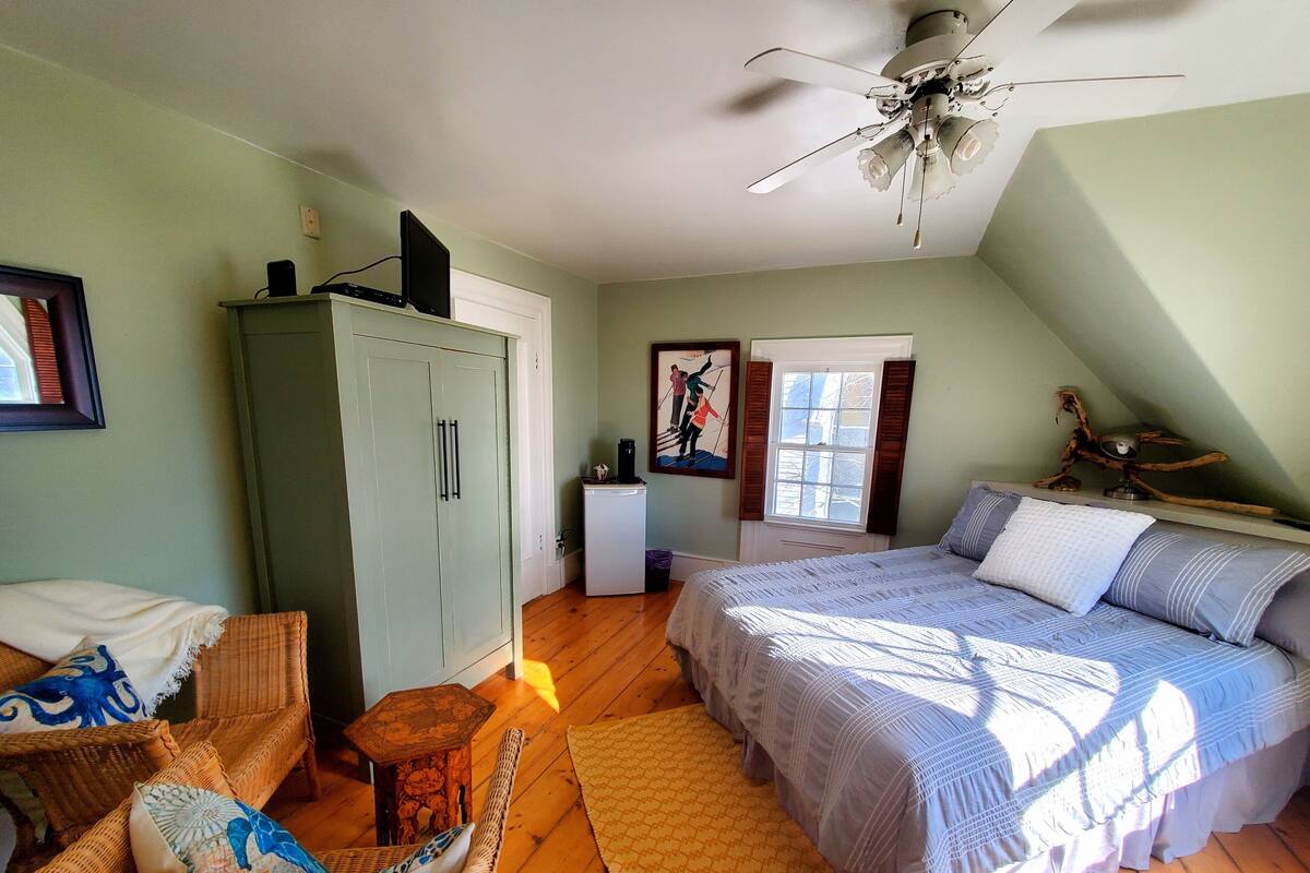 A bedroom with a bed, a chair, a wardrobe, a desk, and a ceiling fan.