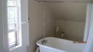 A bathroom with a bathtub, a shower, and a window with shutters.