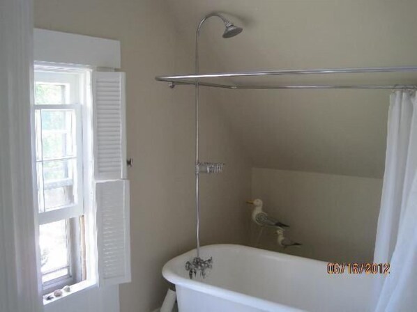 A bathroom with a bathtub, a shower, and a window with shutters. - Fisherman's Daughter Bed & Breakfast (Mahone Bay)