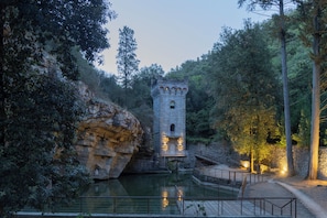 A stone tower with a bridge leading to it, surrounded by trees and a body of water. - Fattoria di Maiano (Fiesole)