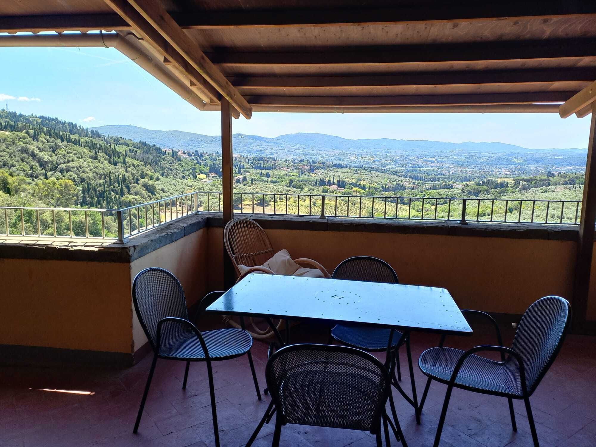 A covered outdoor seating area with a table and chairs, overlooking a scenic landscape.