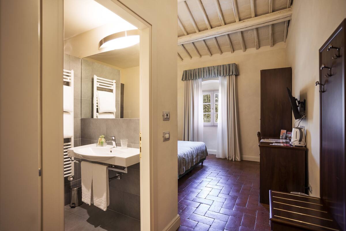 A hotel room with a bathroom, a bed, a desk, and a window with curtains.