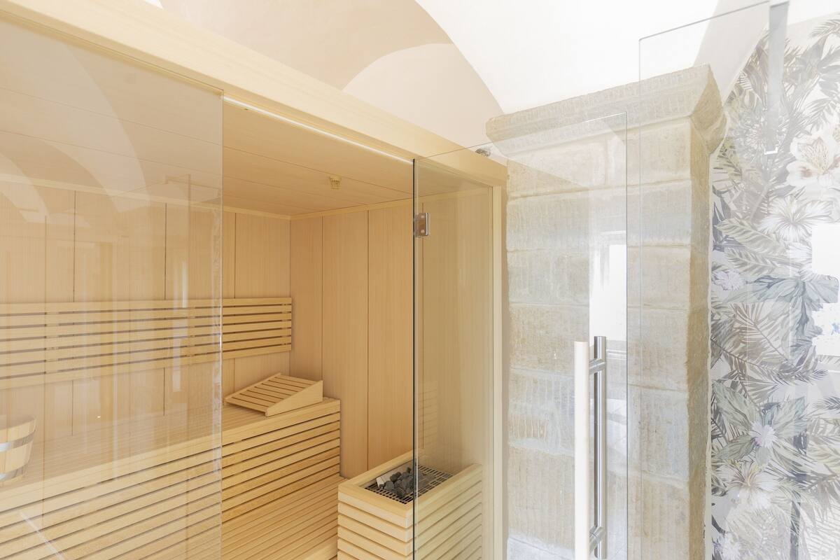 A modern spa room with wooden benches, a glass shower enclosure, and a decorative wall.