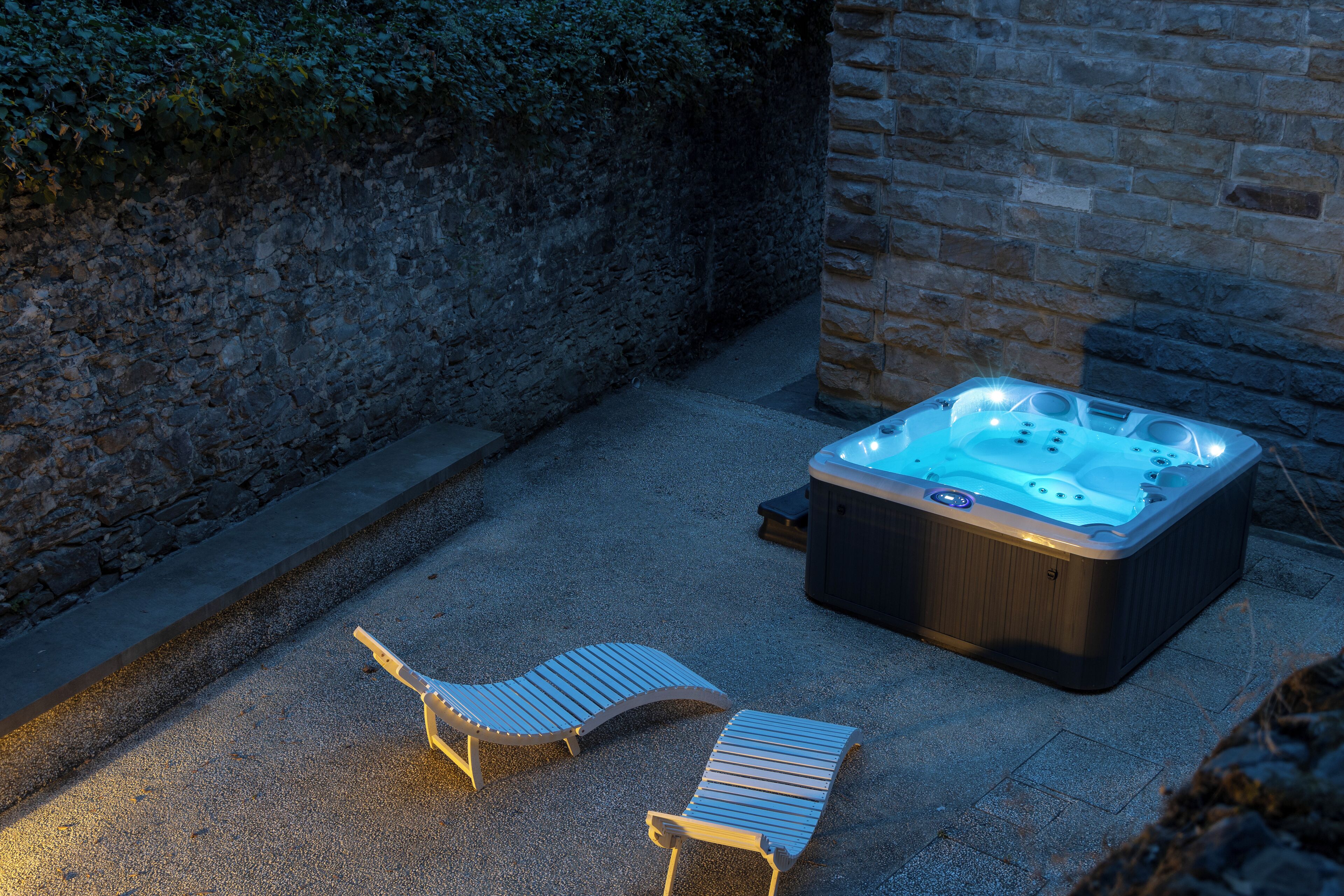 Un jacuzzi con dos sillones de descanso en un área exterior con paredes de piedra.