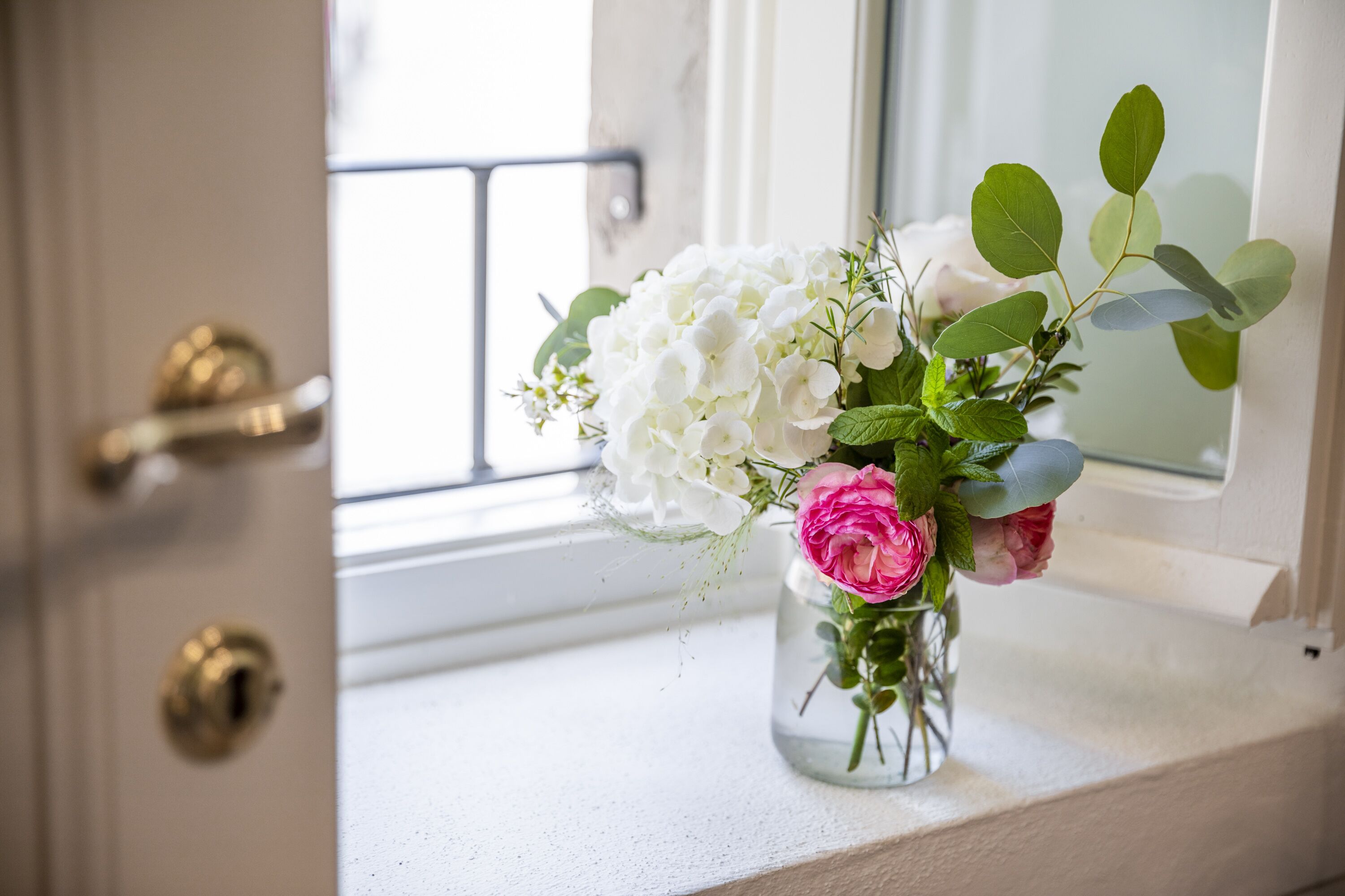 Un vase avec des fleurs blanches et roses, posé sur un rebord de fenêtre.