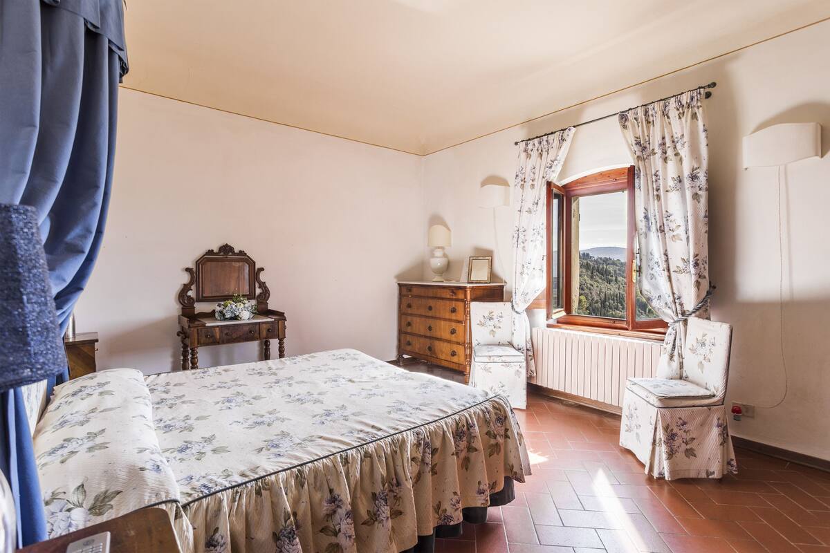 A bedroom with a bed, dresser, chair, window, and radiator.