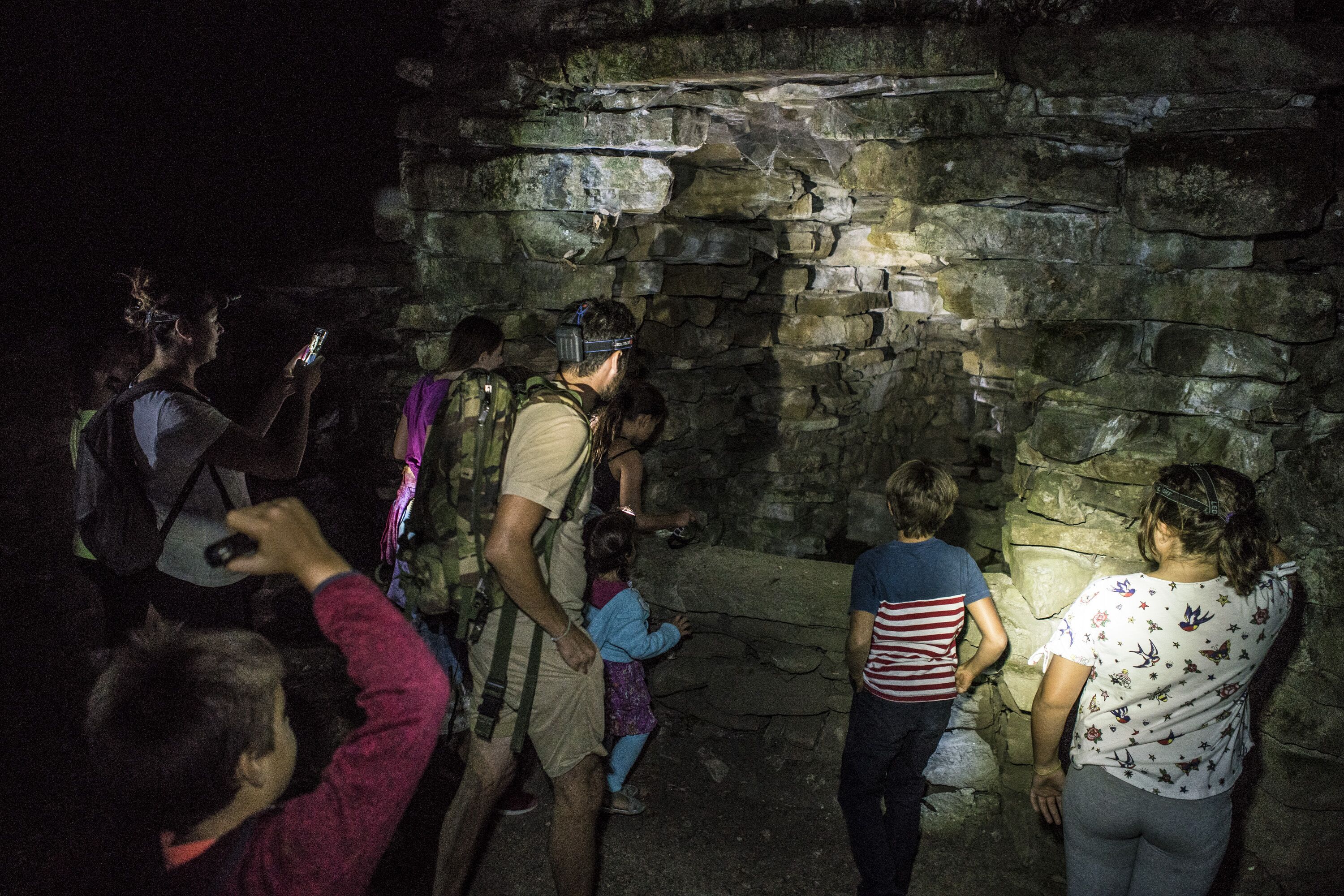 A group of people exploring a stone wall structure in a cave.
