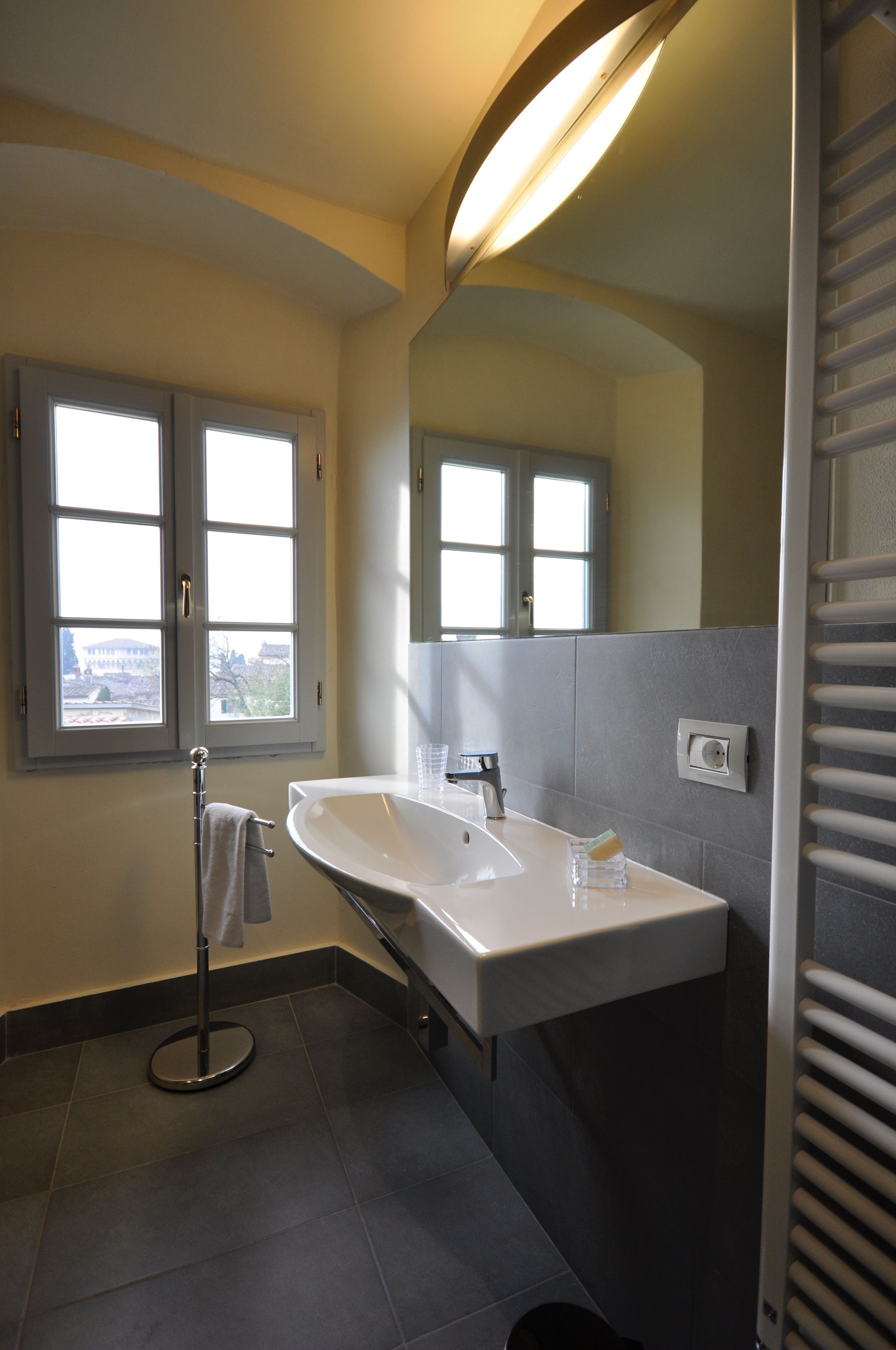 A modern bathroom with a large sink, a towel rack, and a window with a view of buildings.