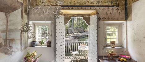 Una habitación con una mesa de vidrio, una silla, una mesita con un florero y una ventana con vista a un jardín.