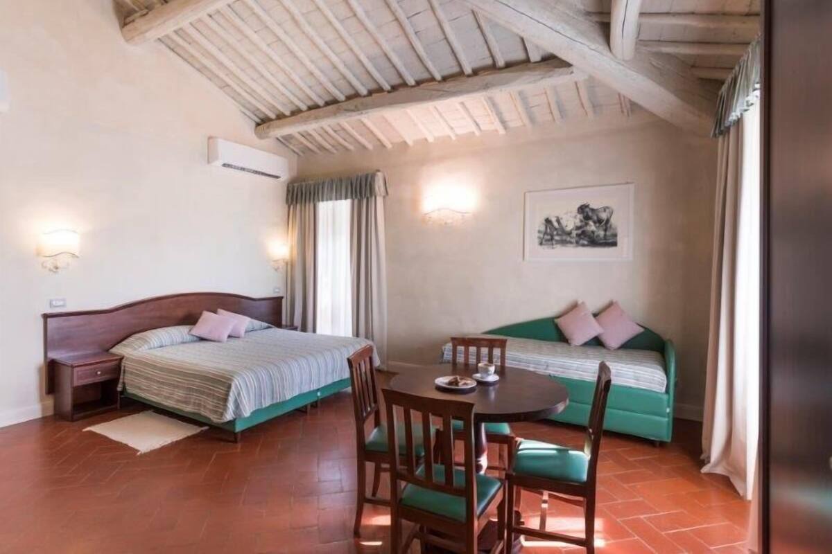 A room with a bed, a sofa, a dining table with chairs, and a ceiling with exposed beams.