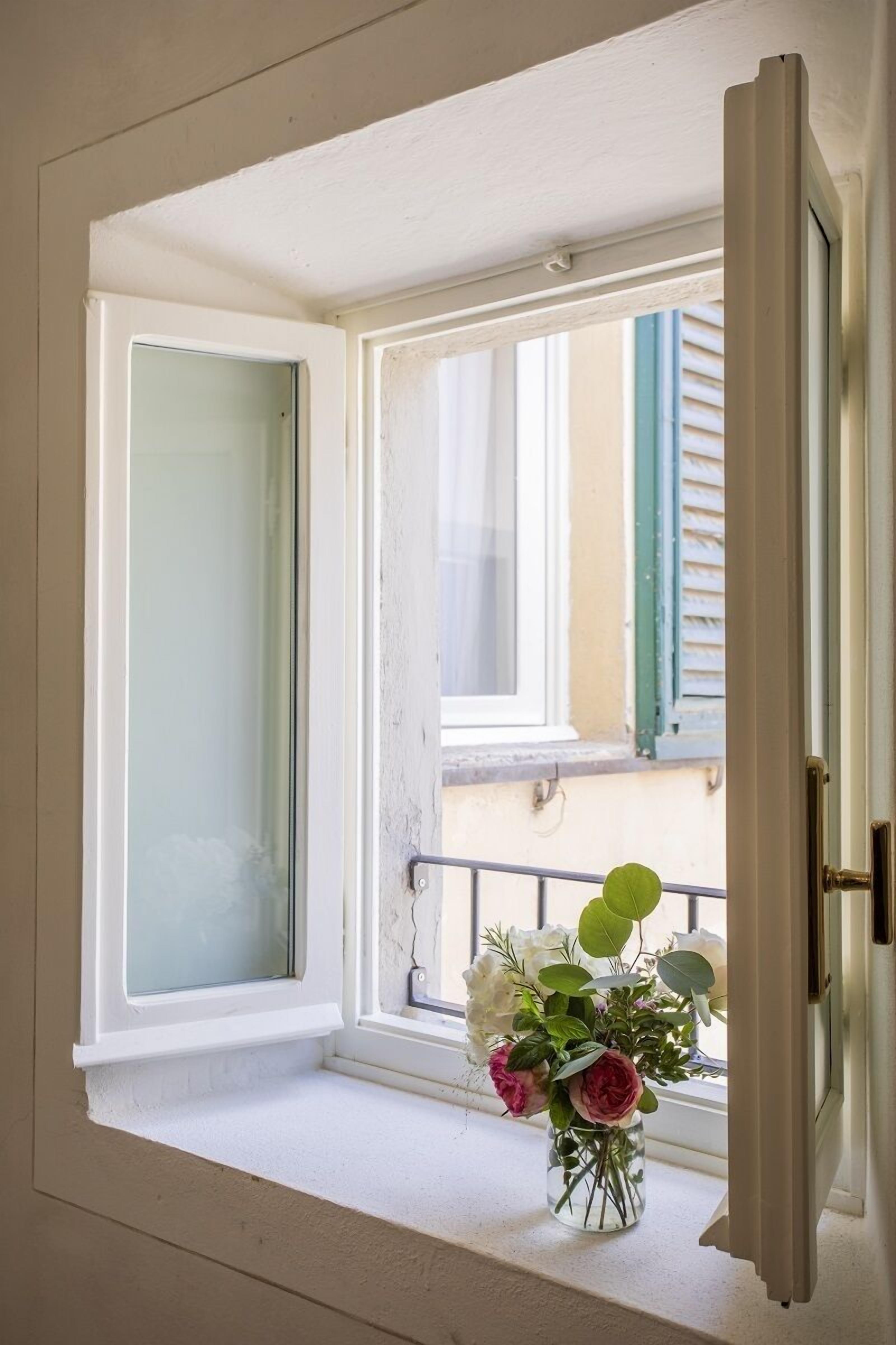 Une pièce avec une fenêtre, une porte et un petit banc près de la fenêtre, sur lequel est posé un vase de fleurs.